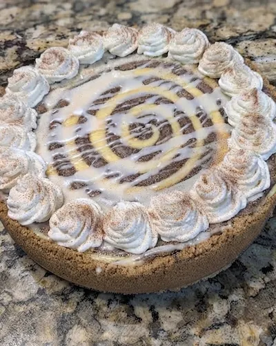 Cheesecake with a graham cracker crust, cinnamon-dusted whipped cream rosettes, and a caramel and vanilla swirl