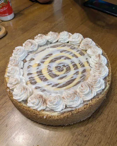 Cheesecake with a graham cracker crust, cinnamon-dusted whipped cream rosettes, and a caramel and vanilla swirl