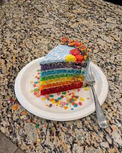 A slice of six-layer rainbow cake with blue buttercream, garnished with fruity cereal pieces