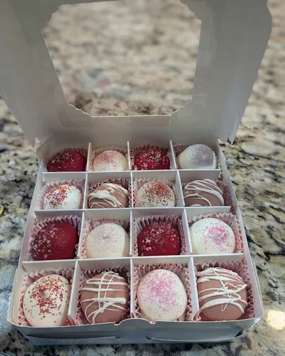 A 16-piece box of hand-decorated chocolate truffles in red, pink, and white with sanding sugar and drizzle detail