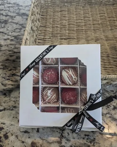 A box of hand-decorated chocolate truffles with white chocolate drizzle and sanding sugar, tied with a Happy Valentine's Day ribbon
