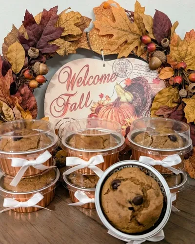 Individually-boxed chocolate chip mini muffins tied with white ribbon, displayed in front of a "Welcome Fall" sign framed with autumn leaves, acorns, and berries